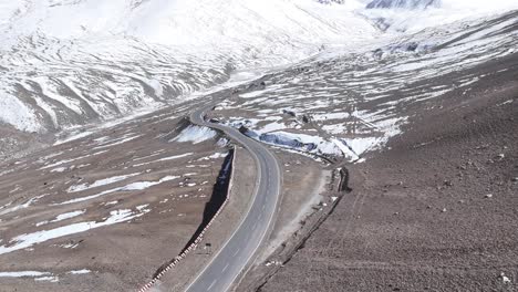 aerial drone shot of a car moving along a serpentine road, framed by snow-capped peaks in ladakh.