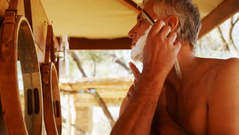 hombre afeitando su barba con una navaja de afeitar en la cabaña 4k