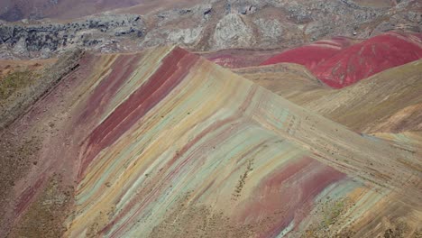 a view of the rainbow mountain hills displaying stripes of red, green, yellow, and brown in peru's highlands on a clear day.