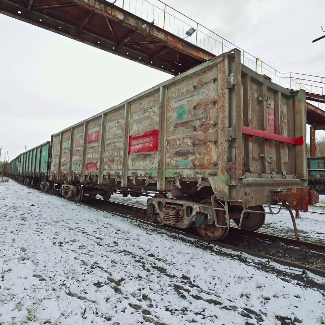 United containers with cargo are moving on rails at the railway station under the bridge on a winter day. Logistics.