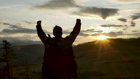 one successful happy travel man standing top joy and raises hands up. joyful silhouette 20s man looking at view sunset sky behind mountains. adventure traveling hike man hands raised on hill closeup