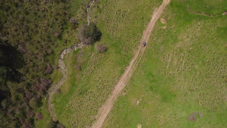 aerial top down shot of buggy car driving on rural sandy path in nature of spain - surrounded by green forest trees during sunny day