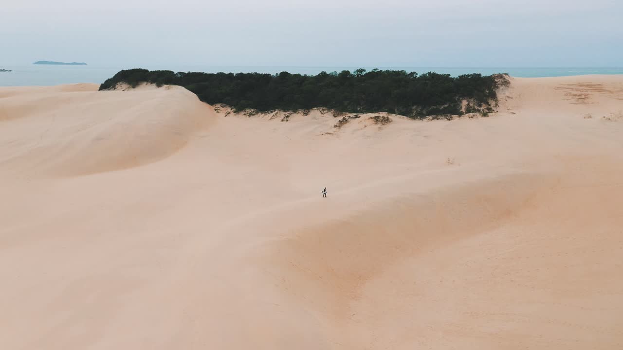 sandboarder caminando solo en grandes dunas de arena cerca de la playa tropical de garopaba, santa catarina, brasil