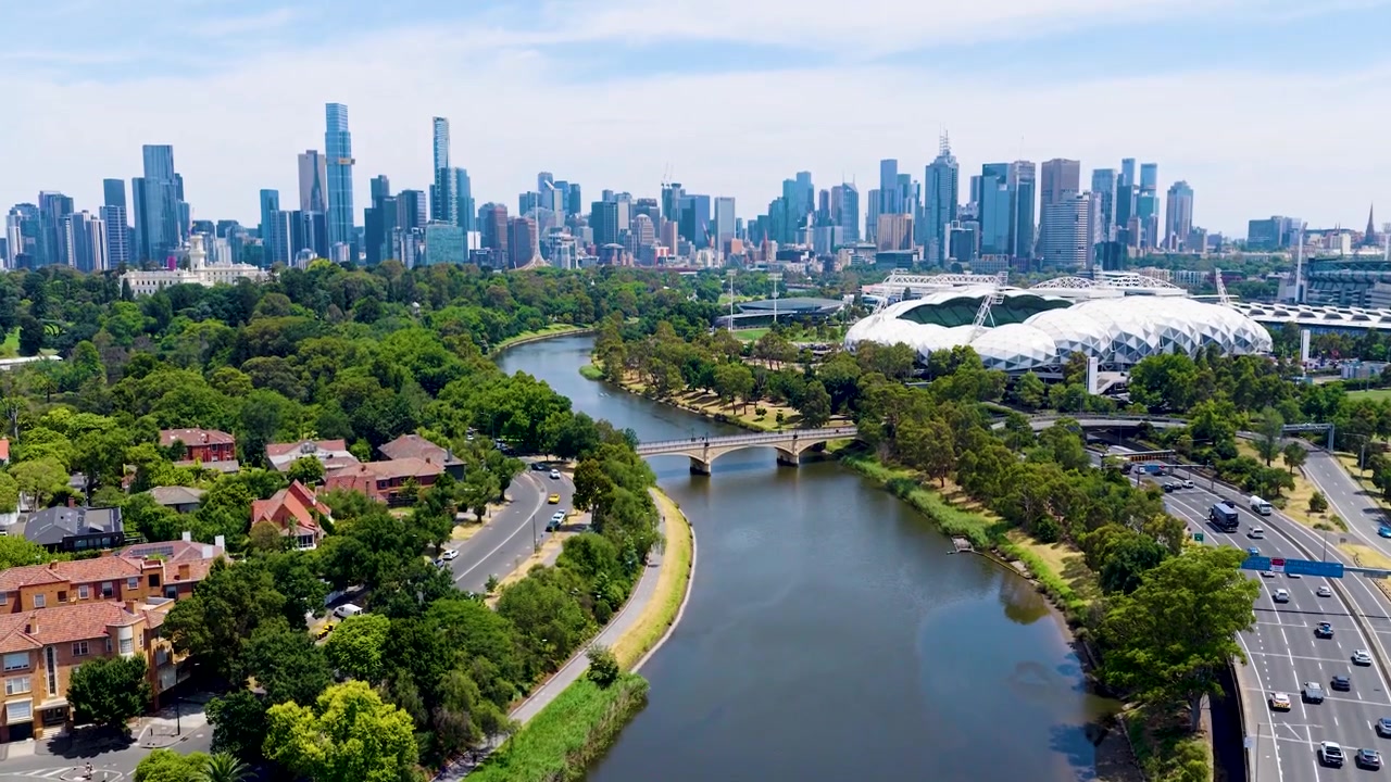 Droneflyvning over Yarra-elven, krysser en bro fra Richmond og Cremorne mot Melbourne sentrum, som avslører elvebreddsstier, frodig parklandskap og byens skyline