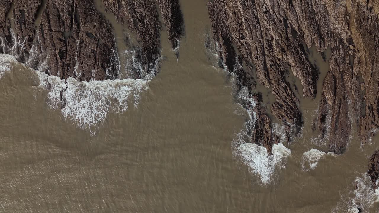 Aerial view featuring muddy Swansea hitting the rocky shore in United Kingdom.