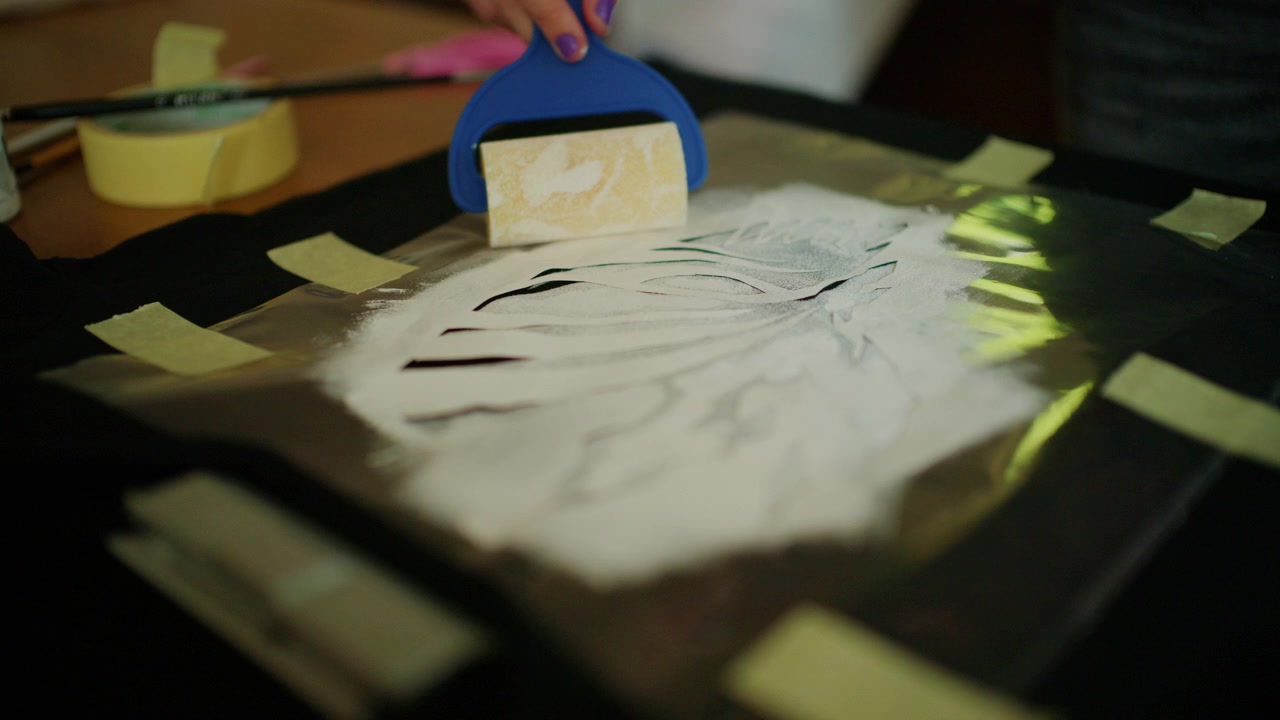 Hands using a craft roller to evenly spread adhesive material over a stencil design