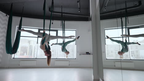 The-interior-shooting-of-an-two-women-practices-different-inversion-antigravity-yoga-with-a-hammock-in-yoga-studio.-The-balance-between-mental-and-physical-two-person-effort-and-achievement-concept