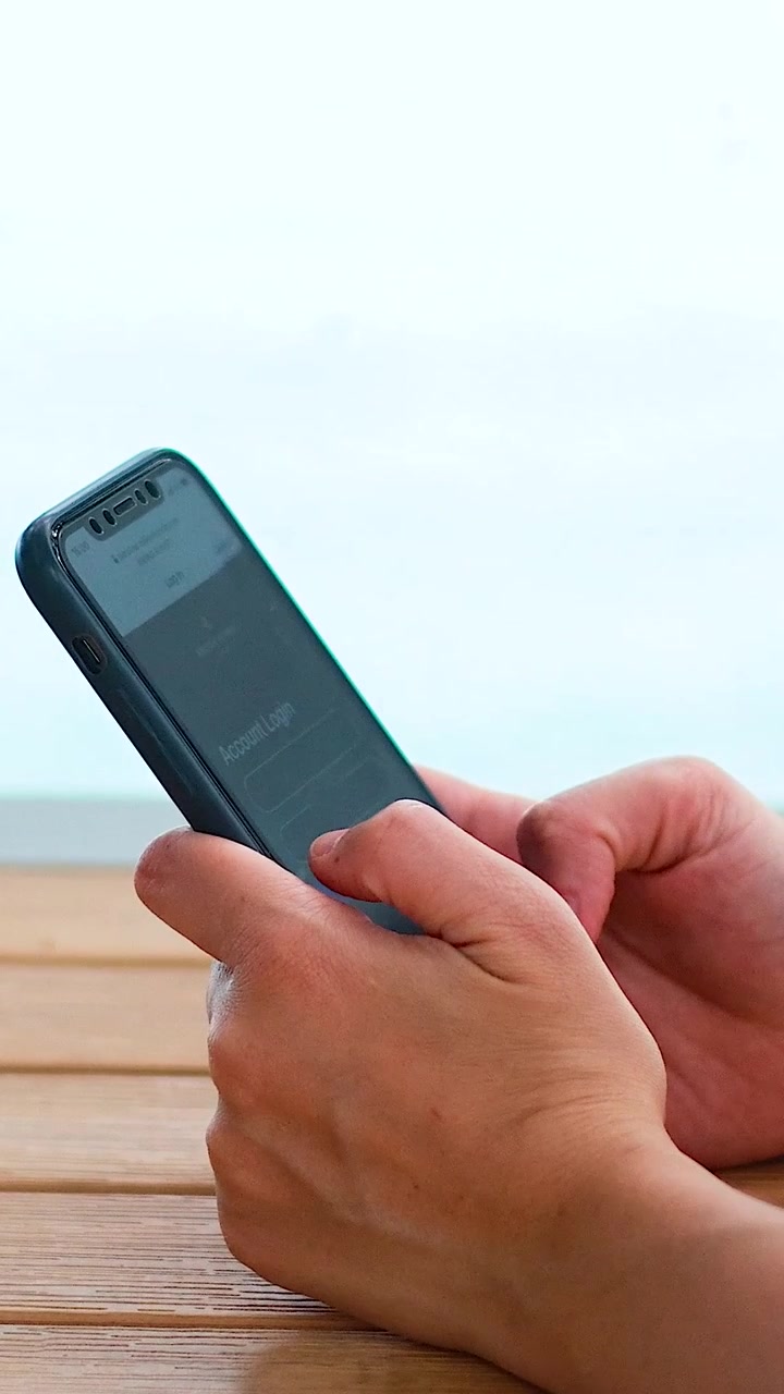 Le mani di una persona interagiscono con lo schermo di un dispositivo mobile su una superficie di legno all'aperto