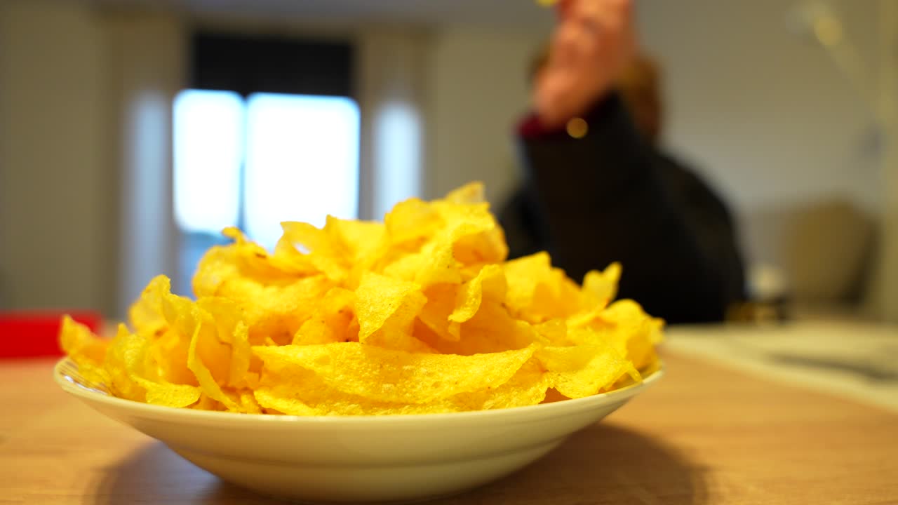 Crispy chips in a white dish on table, people casually snacking in background