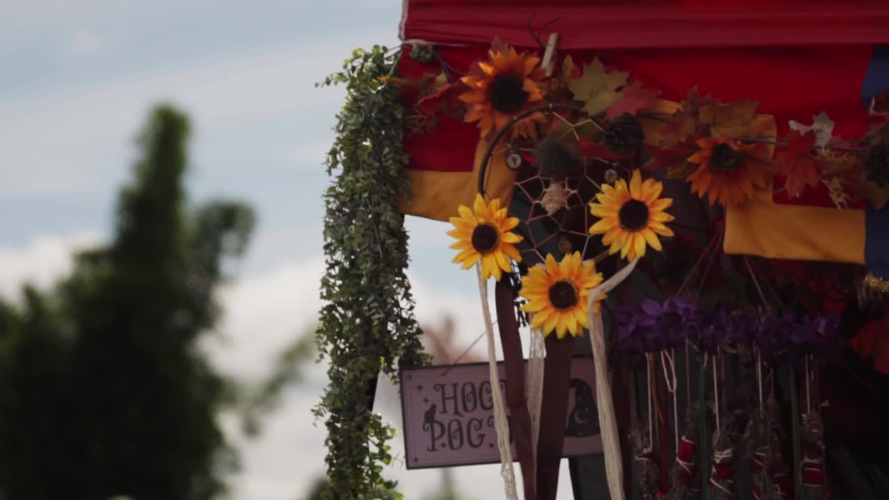 Una vivace esposizione con girasoli, acchiappasogni e vegetazione sotto un baldacchino colorato a un evento all'aperto, con alberi e un cielo luminoso sullo sfondo