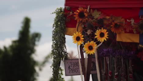 a vibrant display featuring sunflowers, dreamcatchers, and greenery under a colorful canopy at an outdoor event, with trees and a bright sky in the background.