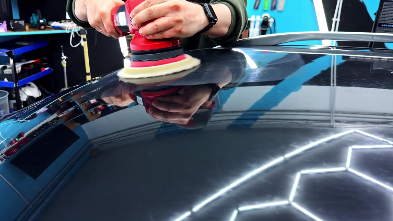 Detalhista polindo o teto do carro com politriz elétrica dentro de uma oficina automotiva, vista de perto.