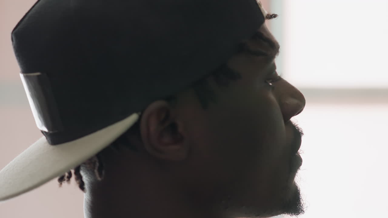 Extreme side view of man wearing cap, head slightly tilted upward, focusing intently on something unseen, with soft blur background highlighting facial profile