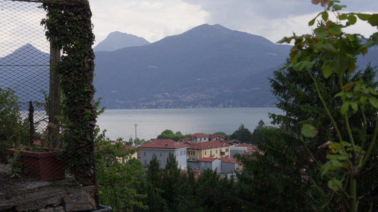Vista panoramica del Lago di Como, Italia, con una terrazza con balcone che si affaccia sull'acqua e sulle montagne circostanti.