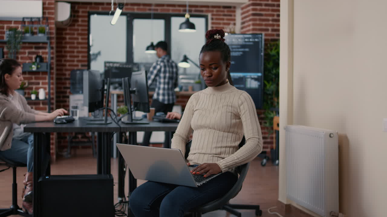 Retrato de um programador afro-americano sentado, programando em um laptop, olhando para cima e sorrindo