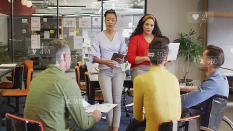 Anmation-of-social-media-icons-over-team-of-diverse-colleagues-discussing-together-at-office