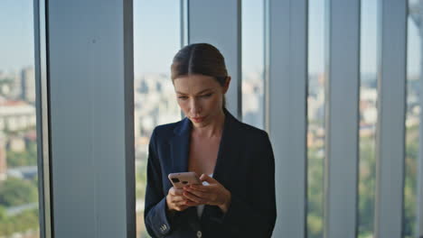 stylish businesswoman messaging mobile phone online in modern office closeup.