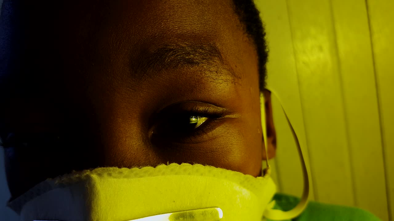 Close-up on a African boy's sad eyes wearing a medical mask.