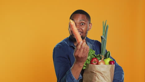 un adulto vegano presenta una zanahoria madura de su bolsa de papel de comestibles