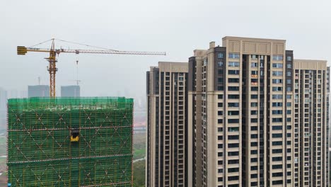 a drone shot of a construction site on the outskirts of chongqing, china, shows a tall residential building under construction. the site is surrounded by scaffolding, machinery, and ongoing work.