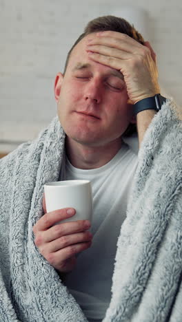 unhappy guy suffering coronavirus infection. sick man covered with warm blanket with a cup of hot beverage staying home. self-isolation and quarantine. vertical video