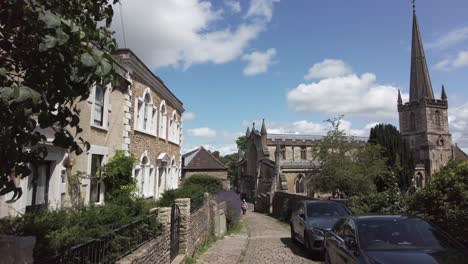 panning towards an old church with a high steeple down a narrow lane in rural england