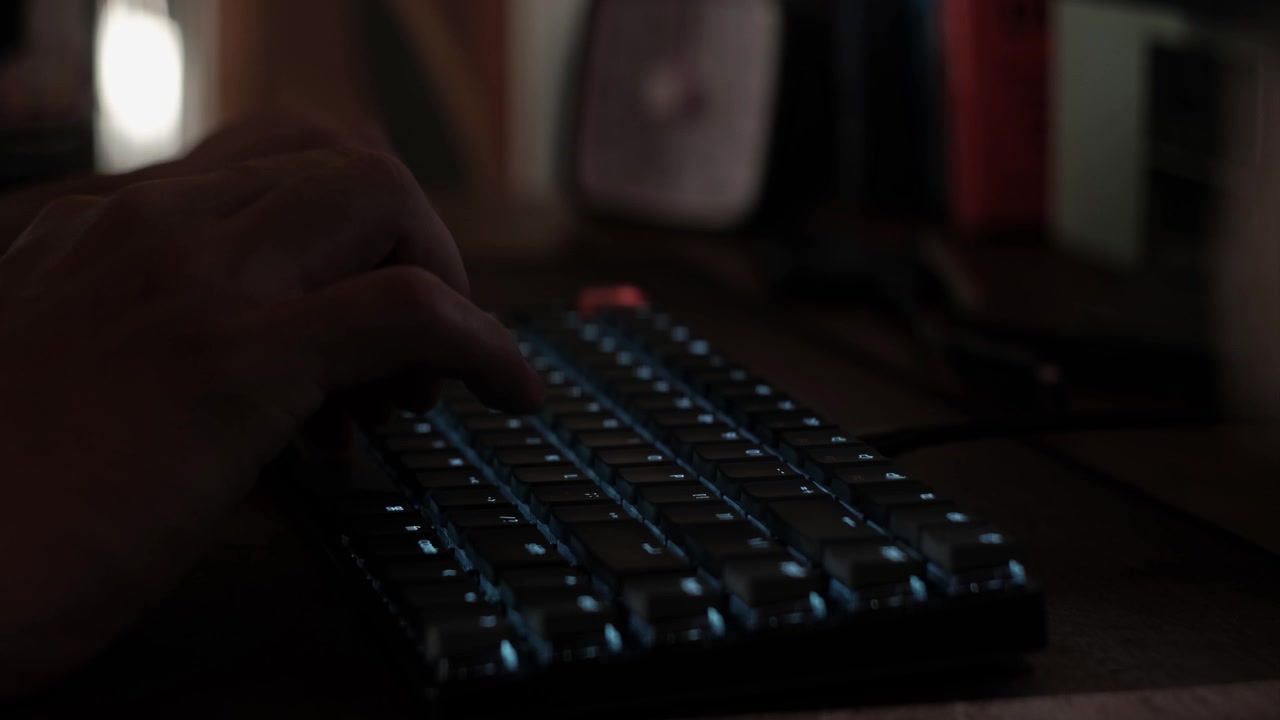 Close-up static shot of hands typing on a mechanical keyboard in a dim workplace setup indoors