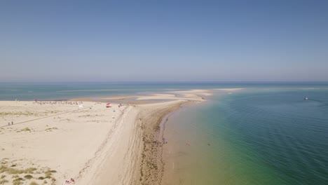 Drone-reverse-above-beach-with-tidal-marks-along-sandy-shores-as-calm-waves-crash-on-beach,-Armona-Island-Olhao