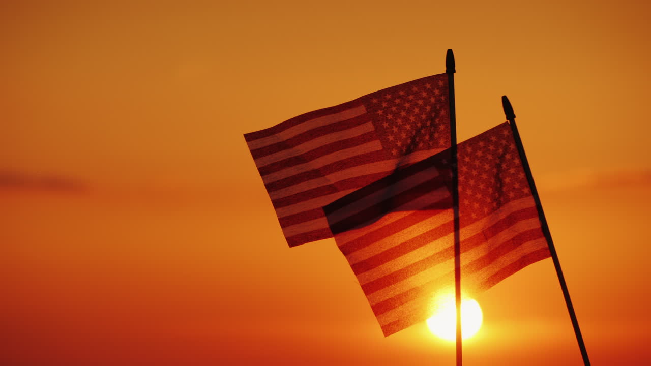 Two American Flags Against The Setting Sun And Orange Sky