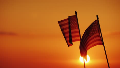 dos banderas americanas contra el sol poniente y el cielo naranja