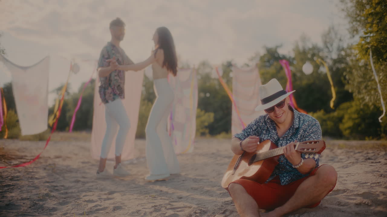 joven feliz tocando la guitarra mientras la pareja baila en la playa