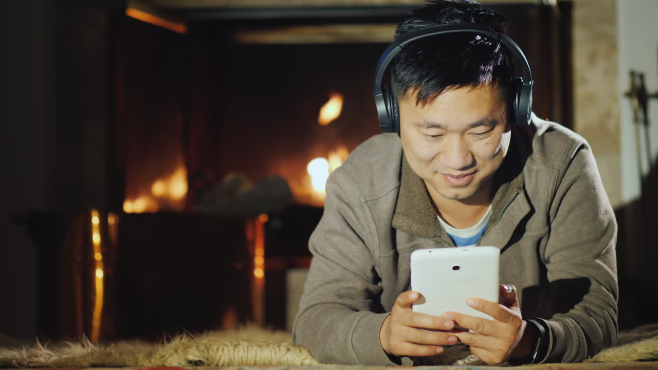 아시아 남자는 벽난로 근처에 태블릿을 사용합니다.