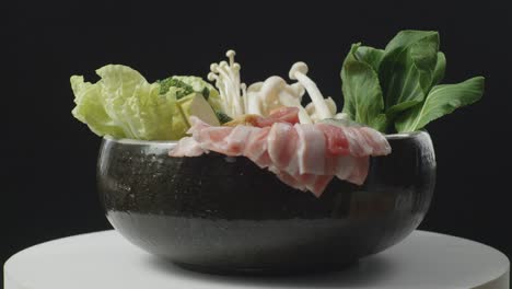 close up of a pot of shabu ingredients spinning around on white table in the black background kitchen