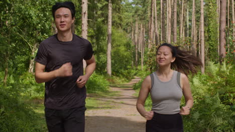 mid adult couple exercising doing work out outdoors running along track through forest towards camera wearing sports clothing