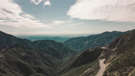 drone time lapse of cars on winding mountain road with view of los angeles skyline from far away and clouds moving by fast