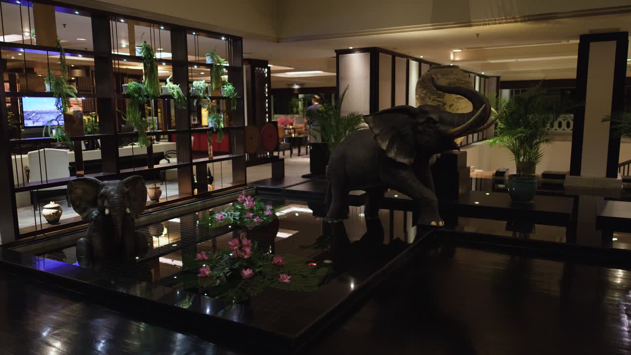 Slow pan reveals elephant statue, lotus flowers, and elegant decor in warmly lit hotel lobby