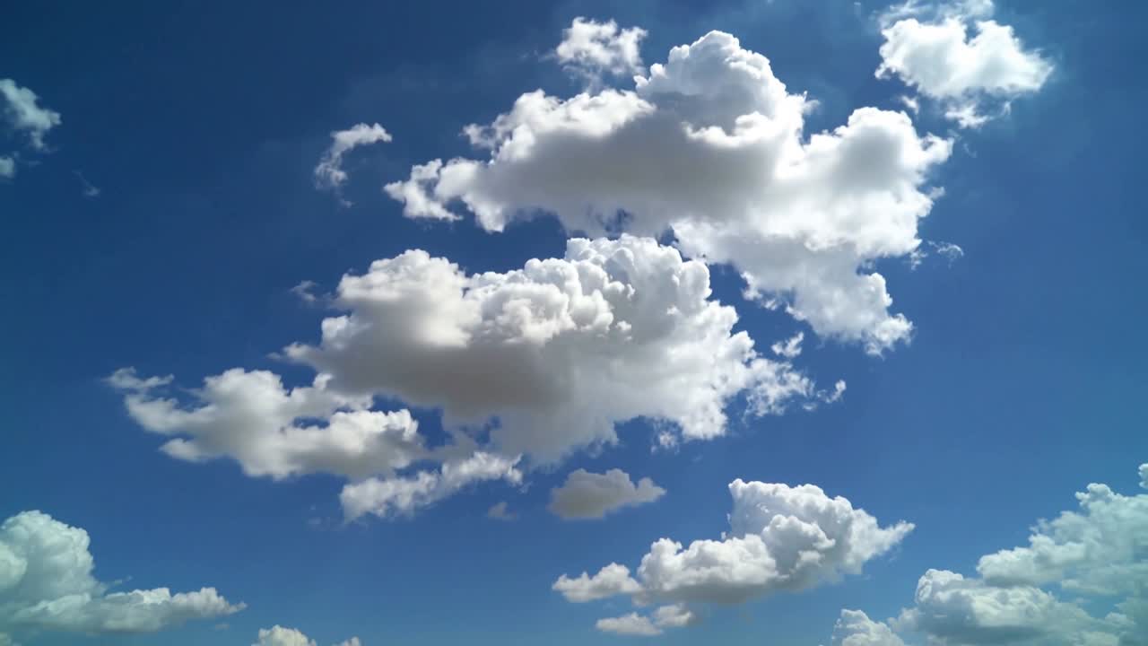 Drifting cumulus cloud billowing upward from sun, driven by wind, small clouds below in blue sky