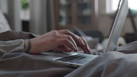 tattooed male hands typing on laptop