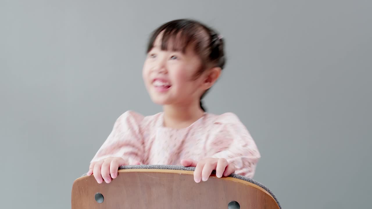 드레스를 입은 귀여운 아시아 소녀가 의자에 앉아 웃고, 웃고, 방에서 행복하게 놀고 있습니다.