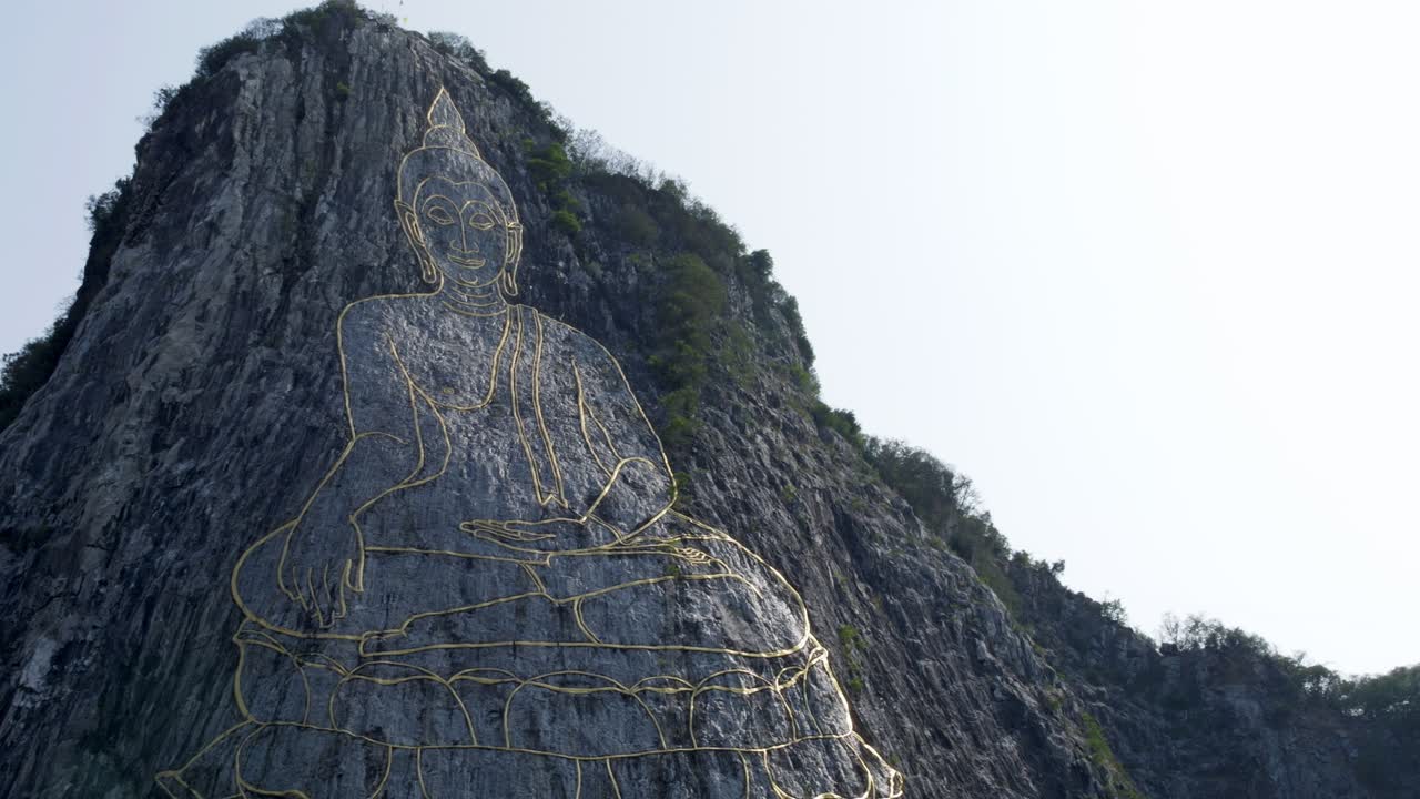 Buddha's Face engraved with gold into the hill in Khao Chi Chan, Thailand. Cinematic footage of Buddha Mountain in Pattaya at dawn. Pan forward to Buddha's golden eyes
