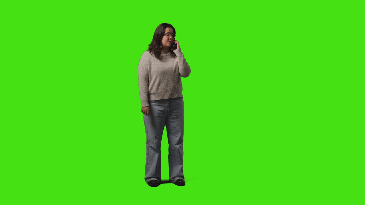 Full Length Shot Of Young Woman Talking On Mobile Phone Standing Against Green Screen Studio Background