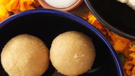 tilt up close up across indian sweets, flowers, diyas on a wooden background for hindu festival of lights, dusshera and diwali preparation and celebration ingredients