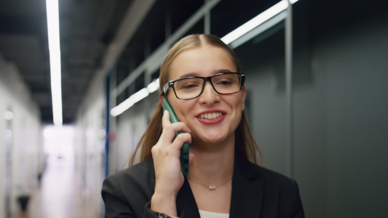 Glad forretningskvinne som snakker i telefonen på kontoret, nærbilde. Smilende leder som går