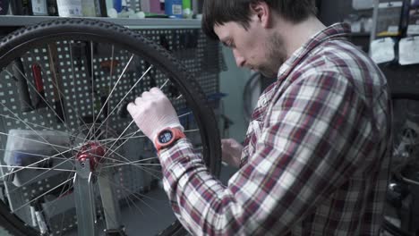 a male bicycle mechanic aligns the tension spokes of a bicycle wheel with a special tool at the workplace in the workshop of a bicycle shop. bicycle maintenance and service. wheel rim alignment tool.