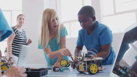 two students with female teacher in after school computer coding class learning to program robot vehicle