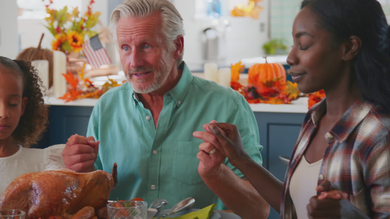 Flergenerationsfamilie, der fejrer Thanksgiving derhjemme og beder inden de spiser måltidet sammen.