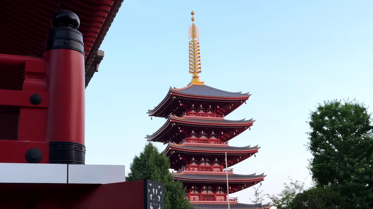 Traditionel japansk pagode med lys rød arkitektur under en klar blå himmel.