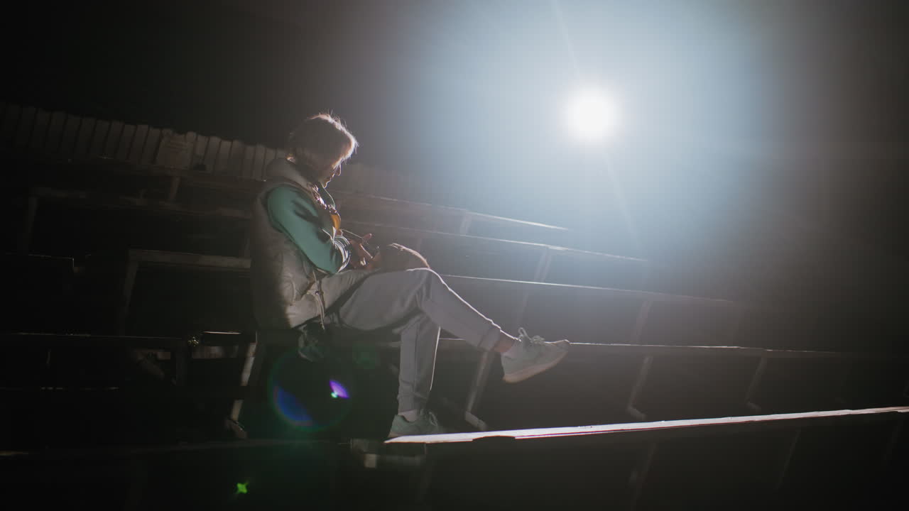 Dog owner seated on stadium benches at night carrying pet dog lovingly on her lap under bright spotlight, creating peaceful emotional bond moment showing warmth, tenderness, and companionship