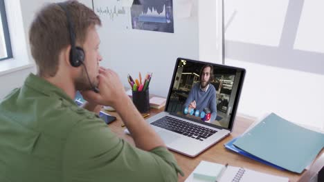 Caucasian-man-using-laptop-and-phone-headset-on-video-call-with-male-colleague