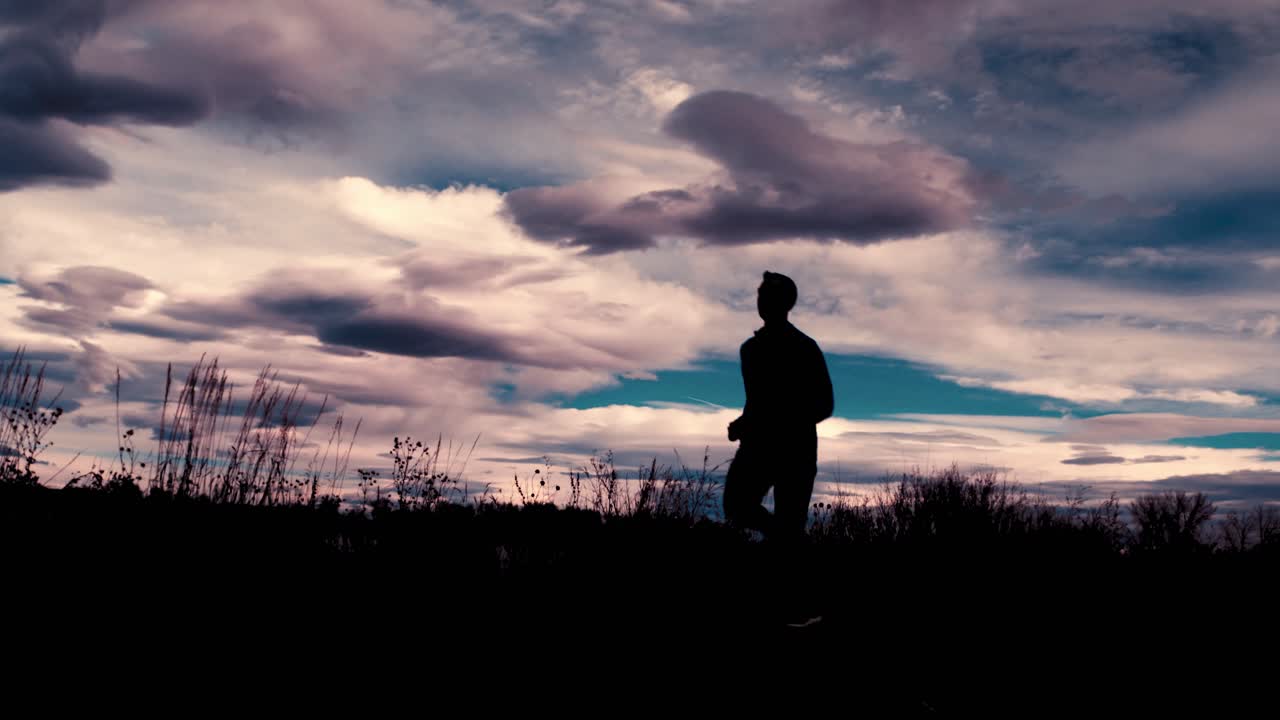 Beautiful black silhouette outline of a male jogger, jogging against a dramatic sky.  The jogger runs toward the camera from right to left.  A wide angle frames this stunning clouds and scenery.